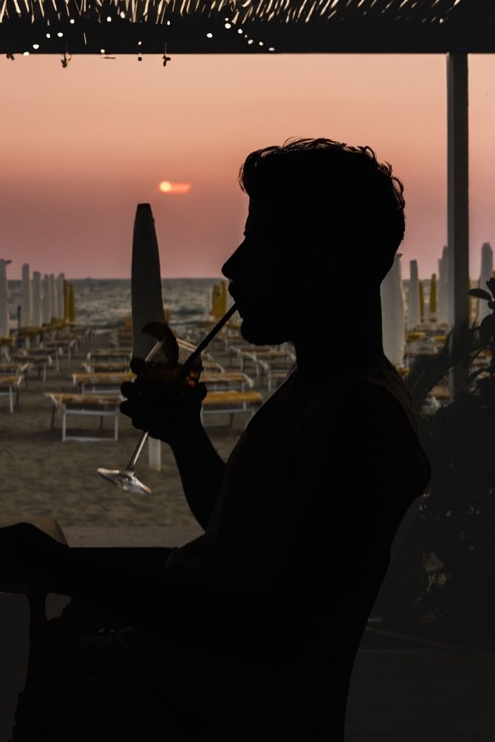 Silhouette di un ospite che beve un calice al tramonto in riva al mare