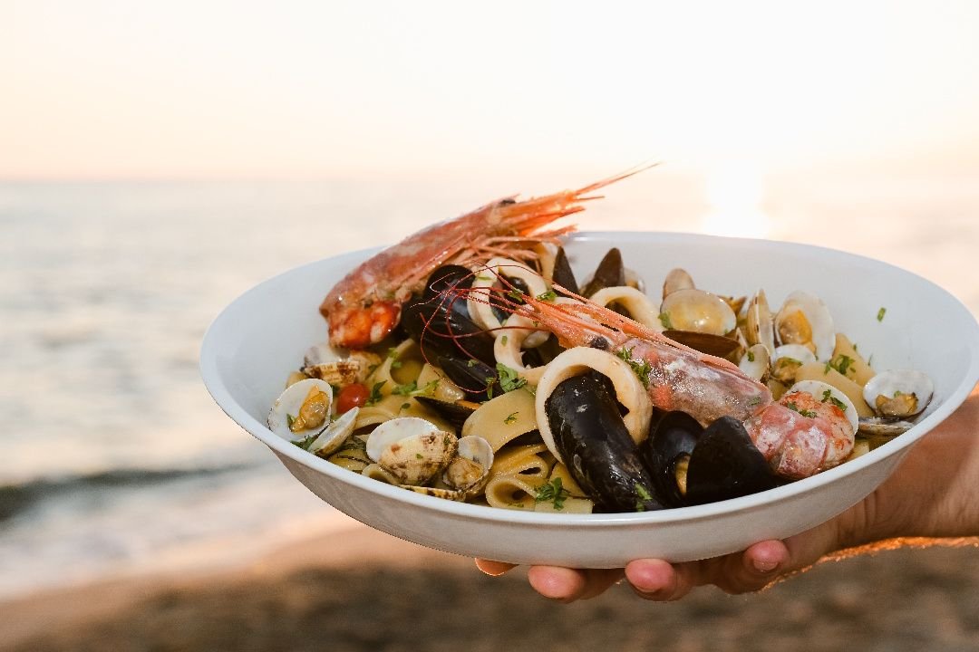Piatto di mezzi paccheri alla pescatora con gambero, cozze, lupini e calamari, tenuto davanti al mare